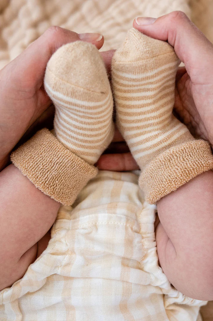 A pair of Organic undyed cotton striped socks made from organic natural color cotton, displayed on a baby's feet.