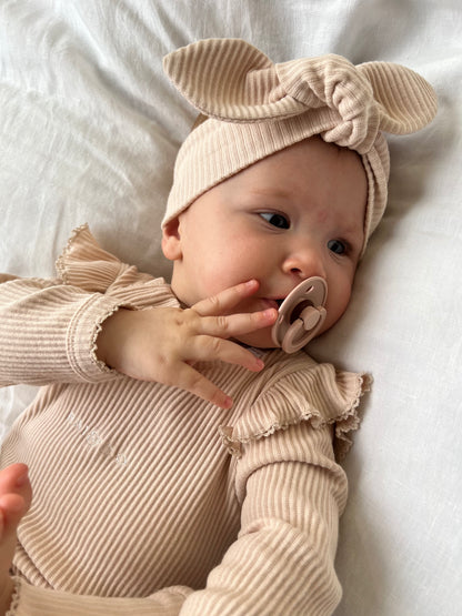 A baby wearing a Ribbed Knotted Headbands in Beige, lying down and sucking on a pacifier.