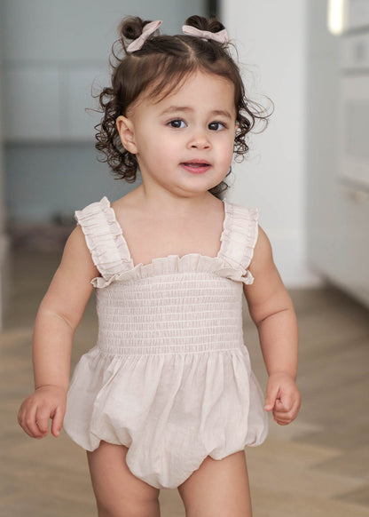Young child wearing a Beige Ruby Romper with ruffled details in a neutral indoor setting