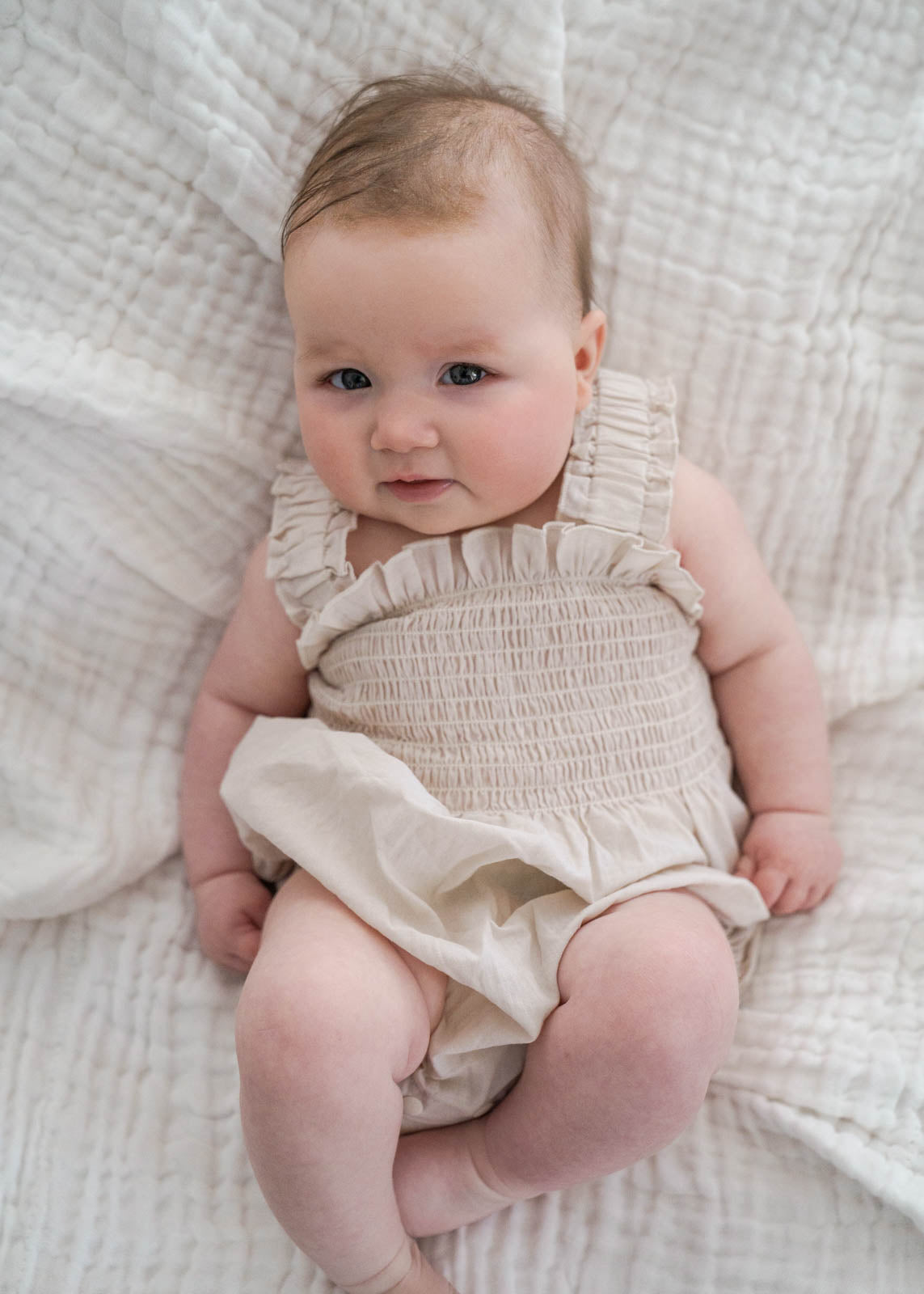 Baby wearing a Beige Ruby Romper lying on a textured white blanket