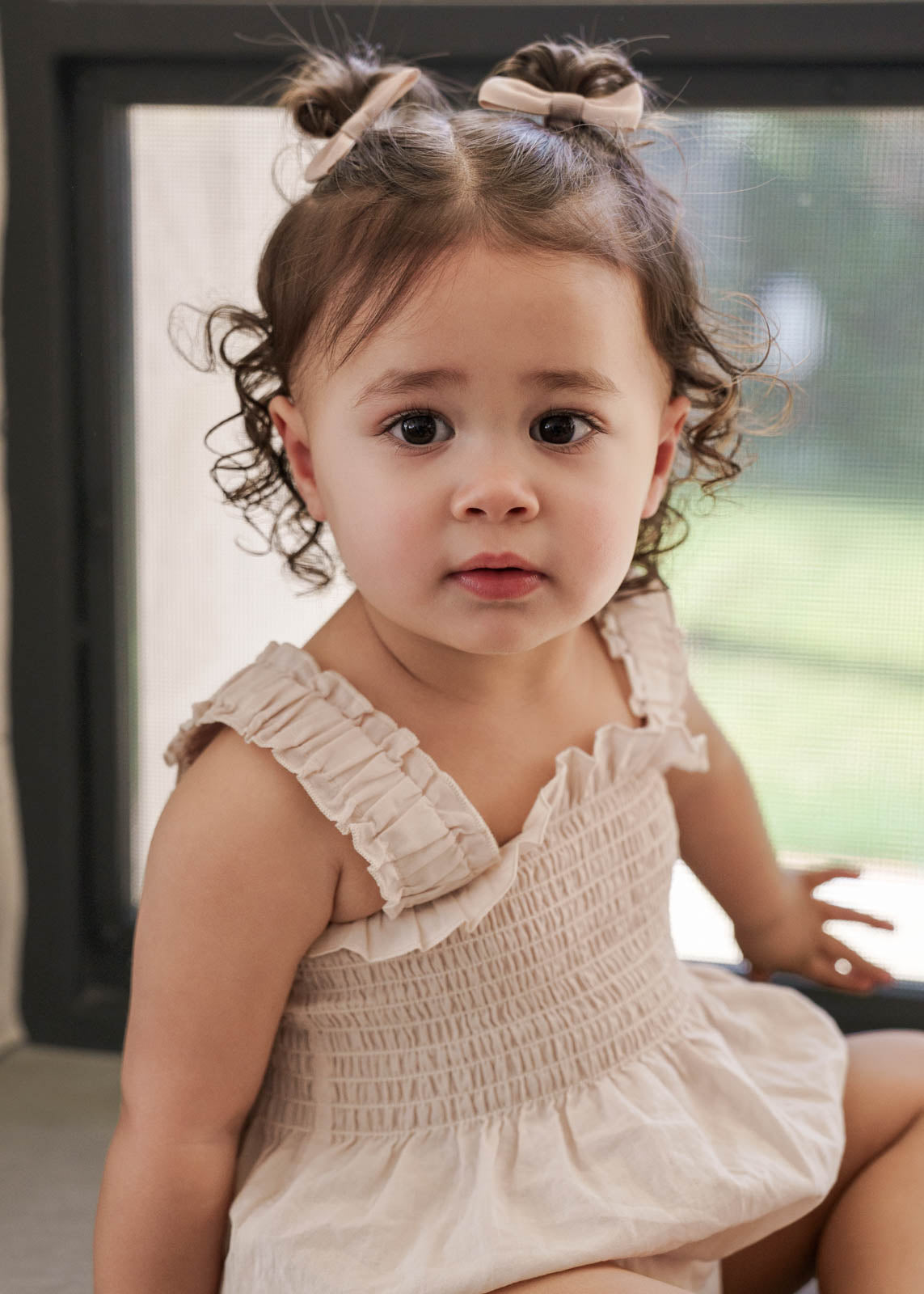 Young girl in a Ruby Romper Beige sitting indoors.