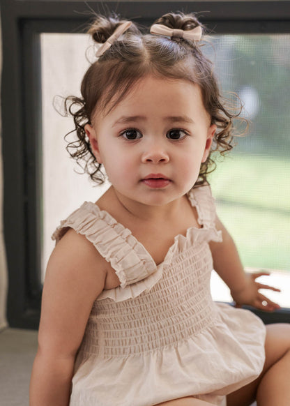 Young girl in a Ruby Romper Beige sitting indoors.
