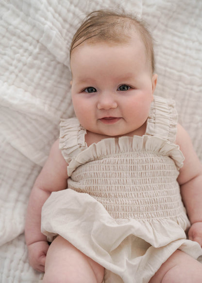 Baby wearing a Ruby Romper Beige lying on a textured white blanket