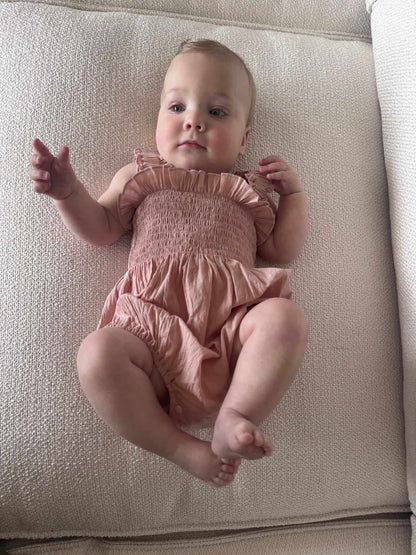 Baby in a Pink Ruby Romper lying on a beige couch