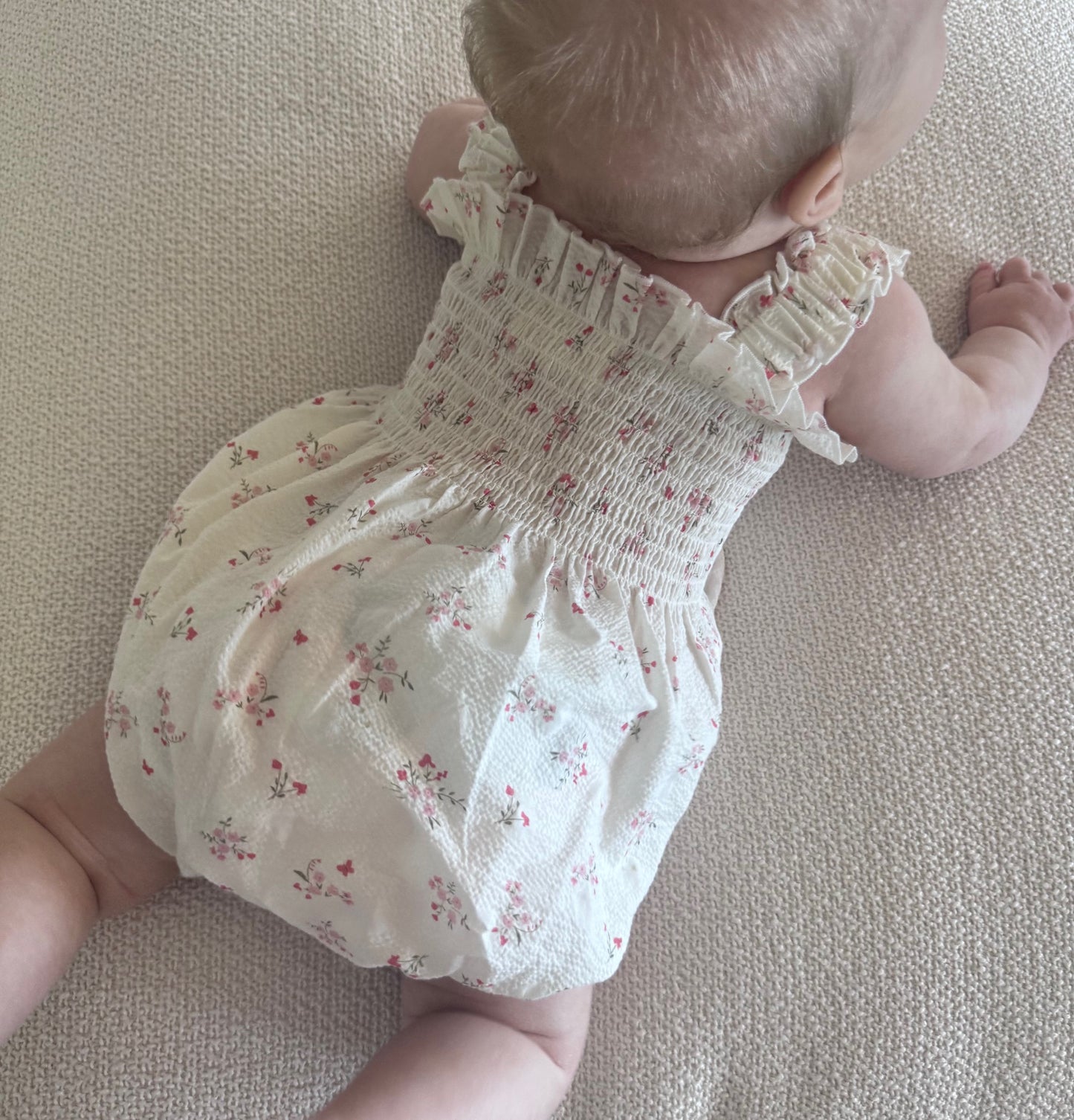 Baby in a White Floral Ruby Romper lying on a beige surface
