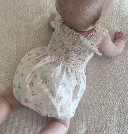 Baby in a White Floral Ruby Romper lying on a beige surface