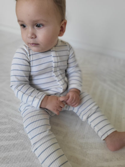 A baby wearing a Striped Onesie in Blue sitting on a light background.