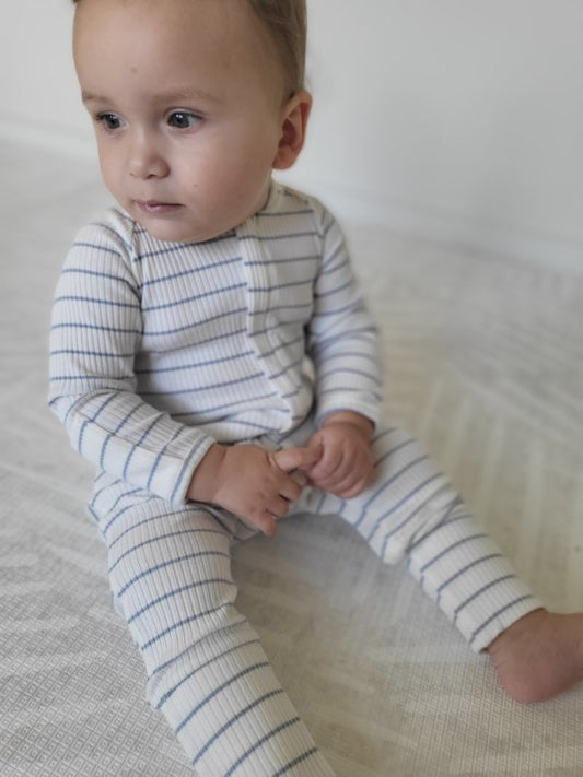 A baby wearing a Striped Onesie in Blue sitting on a light background.