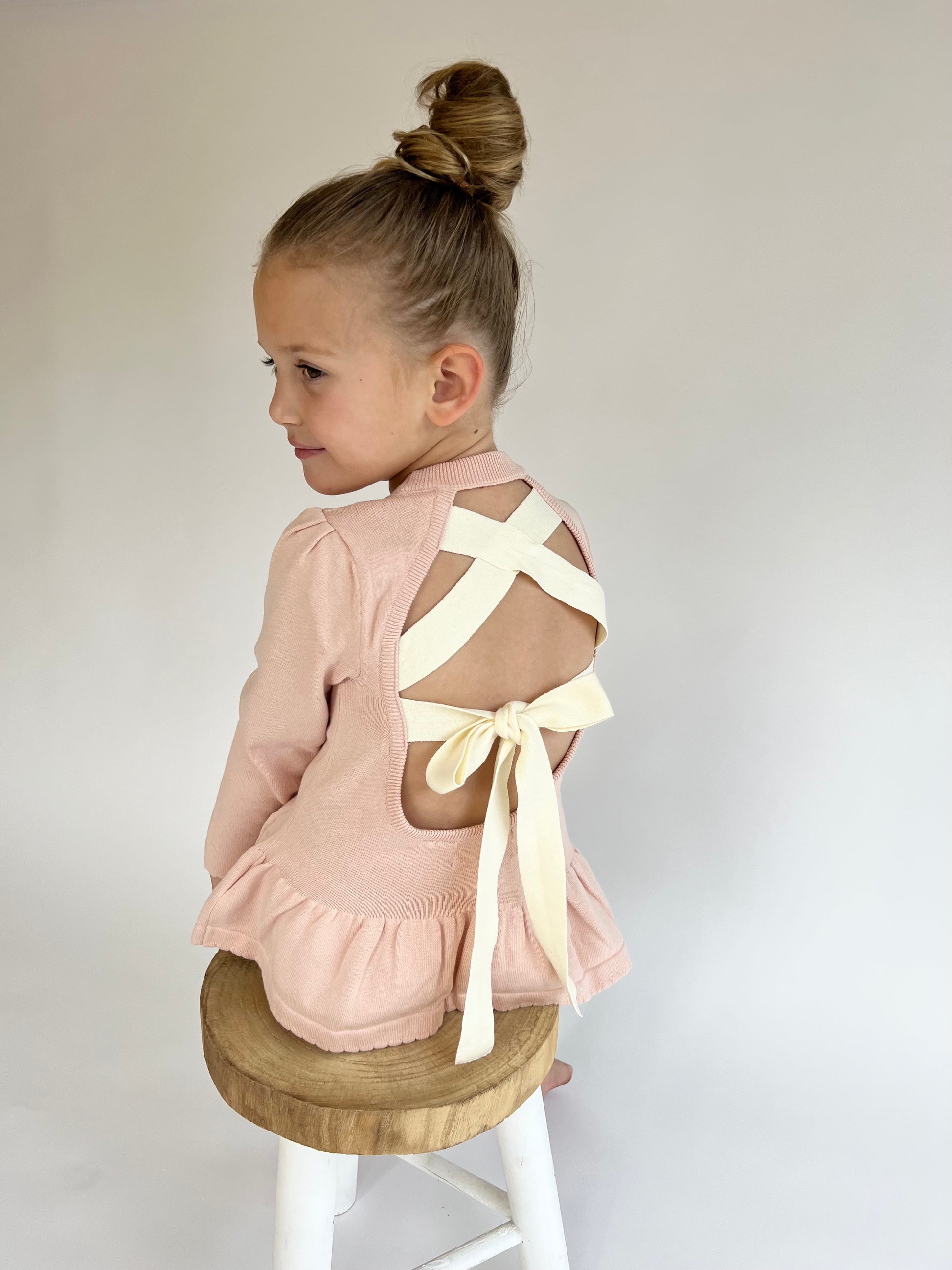 A young girl wearing a Ballerina Top, standing on a white stool.