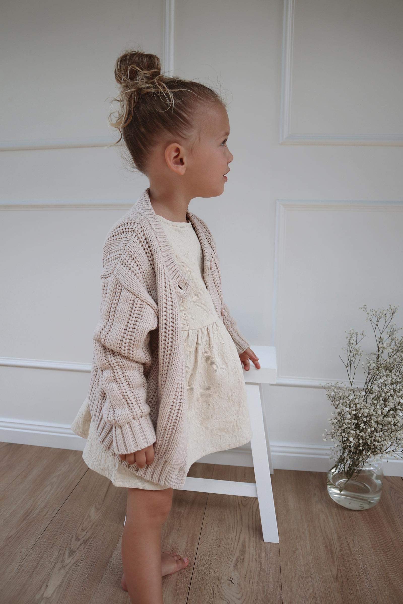 A young child wearing a Chunky Knitted Cardigan in Beige 