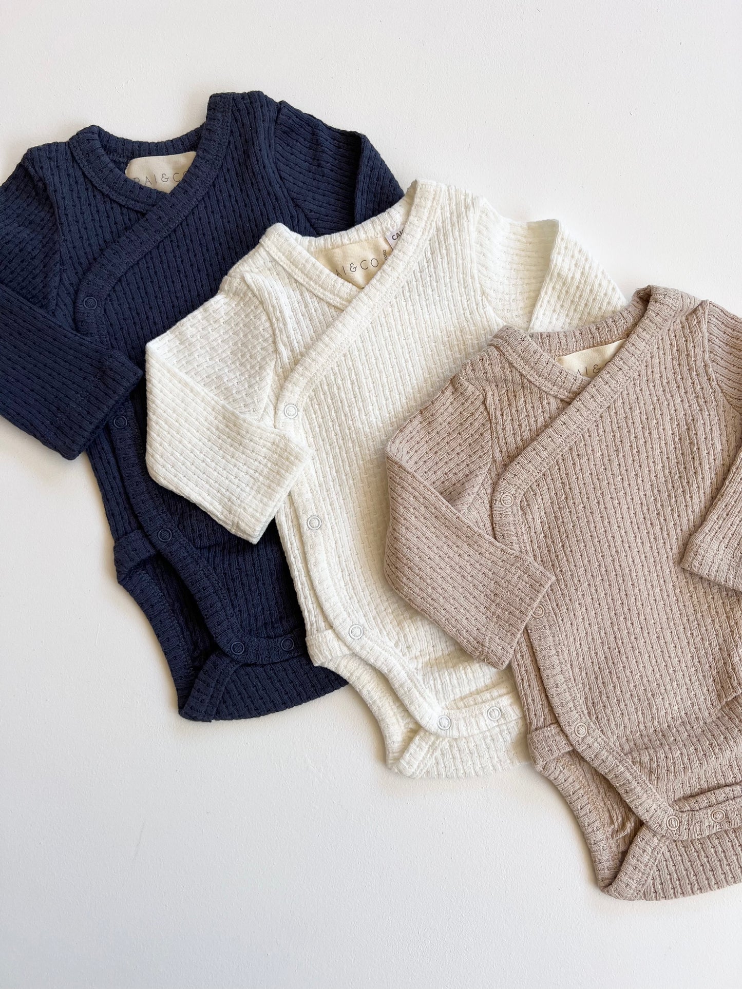 Three Knitted Button Kimono in Available Colours for babies laid out on a flat surface.