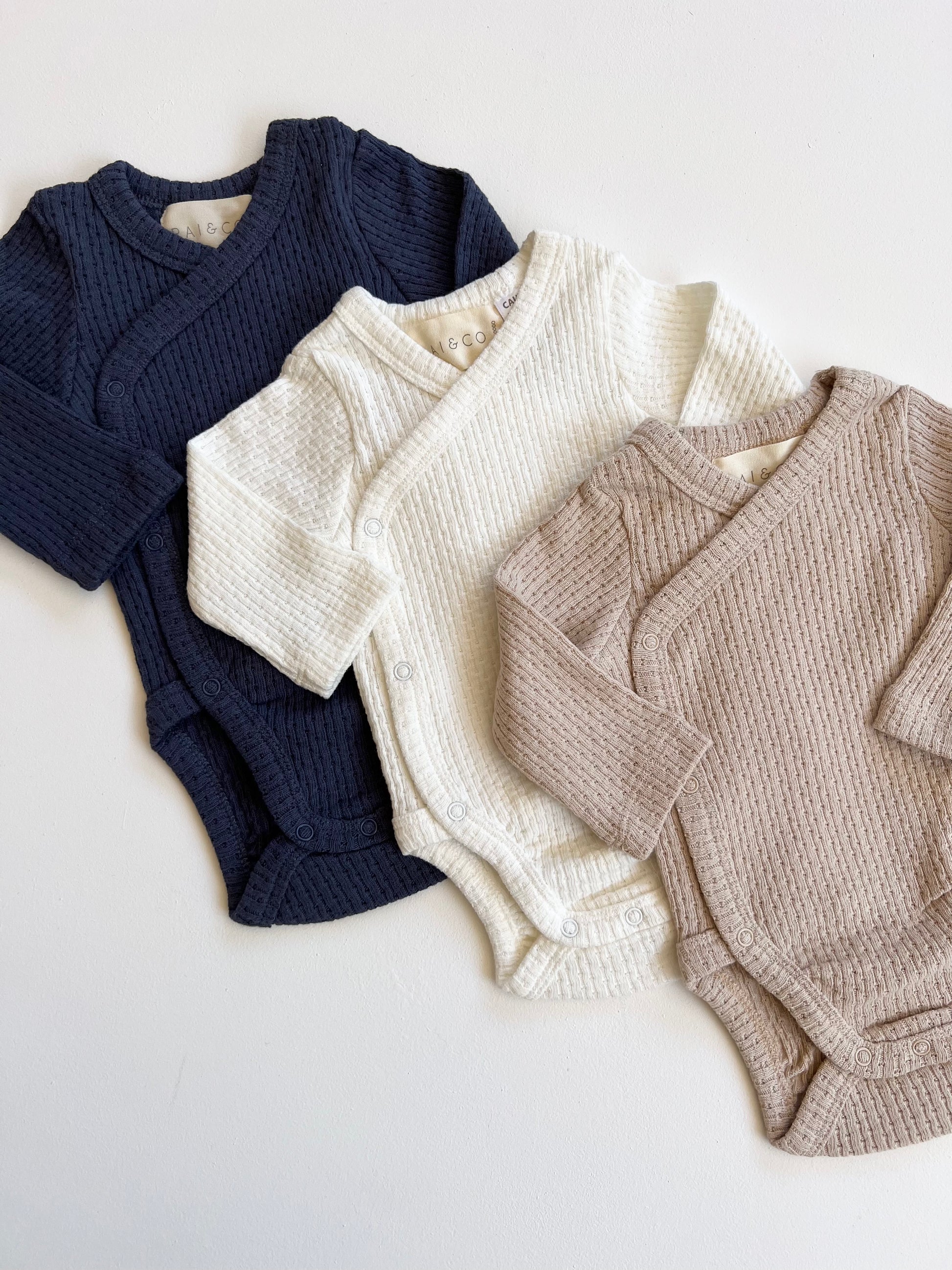 Three Knitted Button Kimono in Available Colours for babies laid out on a flat surface.