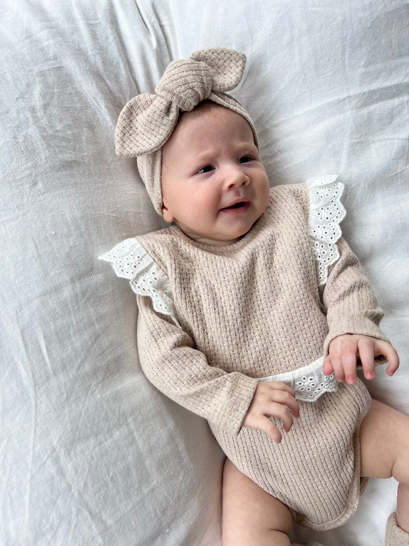 Baby wearing a Knitted Knot Headband in Beige on a white bed