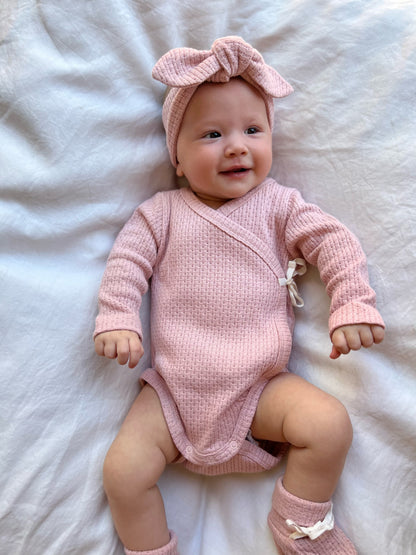 Baby wearing a Knitted Knot Headband in Pink on a white bed
