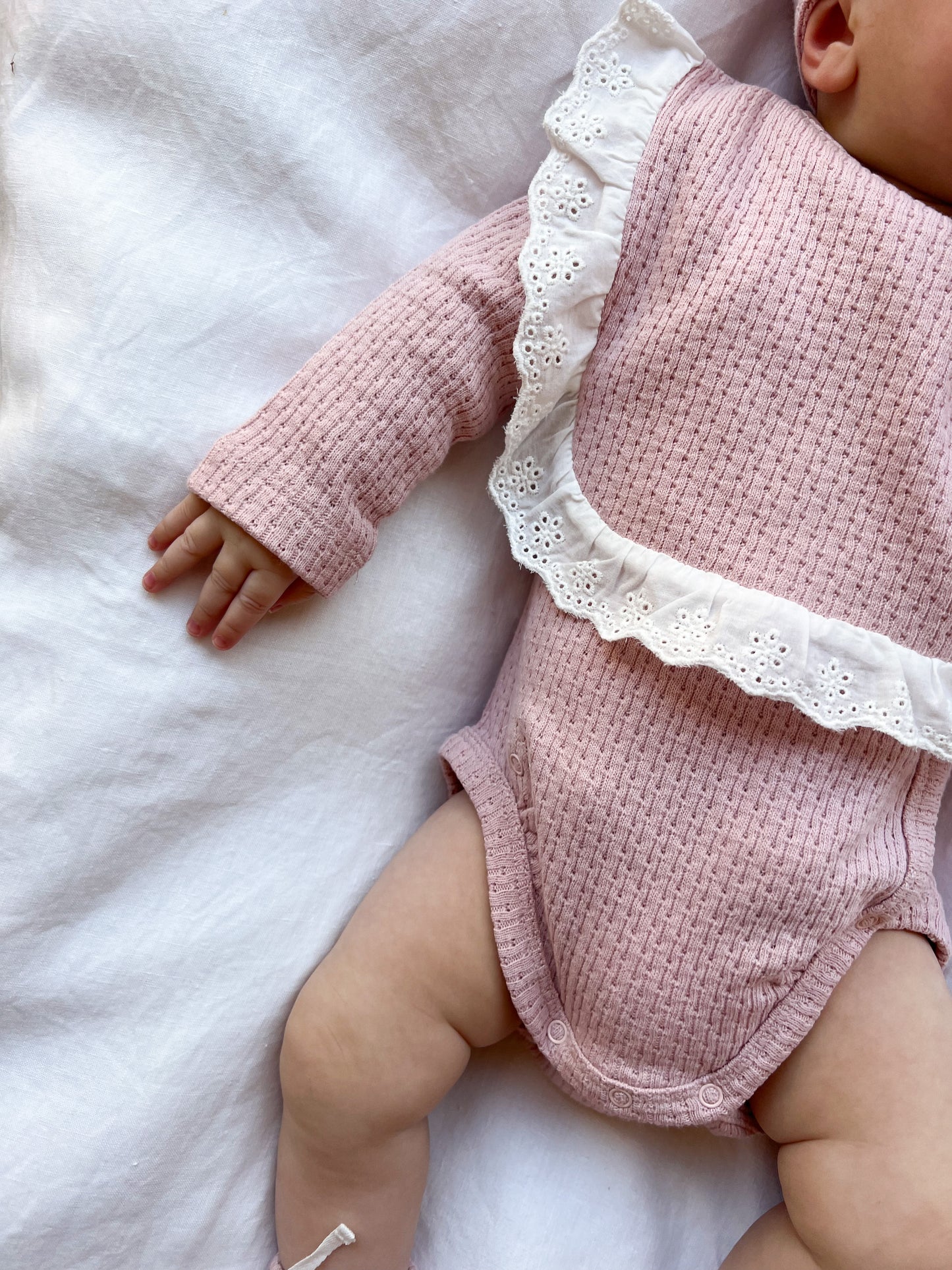 Baby wearing a Knitted Lace Frill Bib in Pink on a white background
