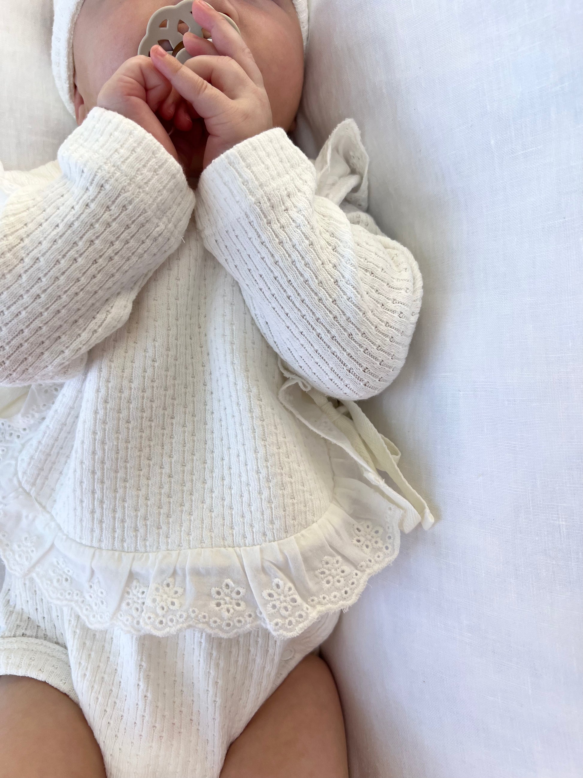 Baby wearing a Knitted Lace Frill Bib in White on a white background