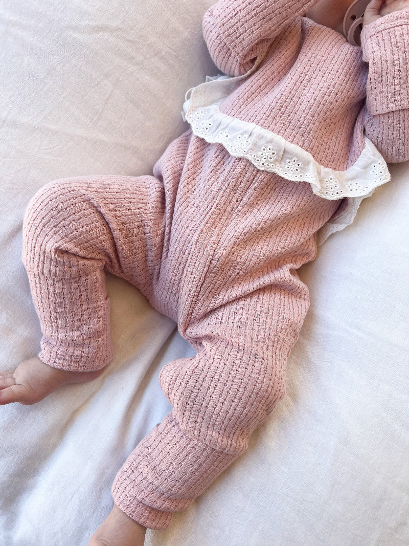 close up Knitted Onesie in Pink on a white bed