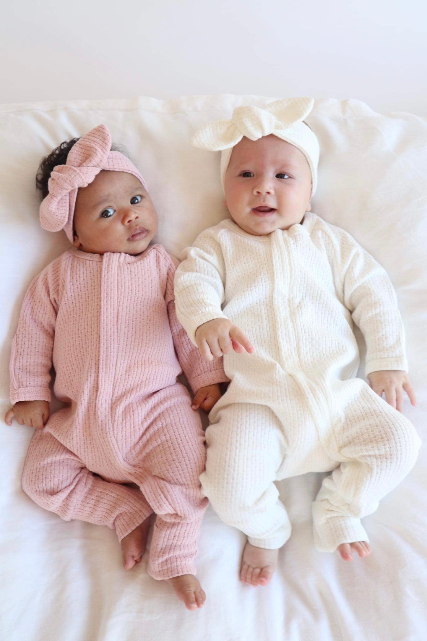 two babies wearing a Knitted Onesie in White and Pink on a white bed