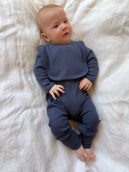 Baby wearing a Knitted Plain Bib in Navy lying on a white bed