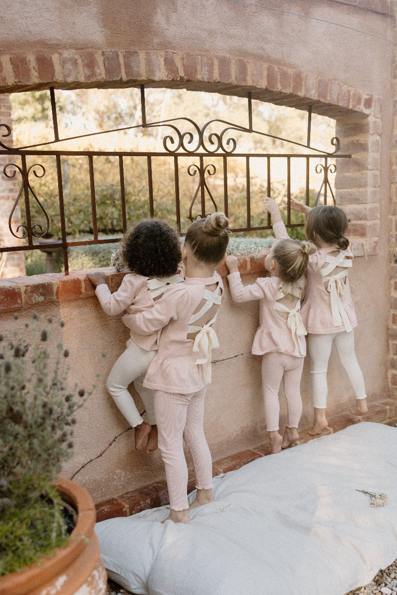 four young children wearing Mini Ribbed leggings in Available Colours, standing and playing with a decorative fence in the background.