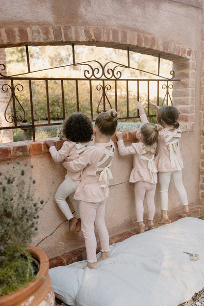 four young children wearing Mini Ribbed leggings in Available Colours, standing and playing with a decorative fence in the background.
