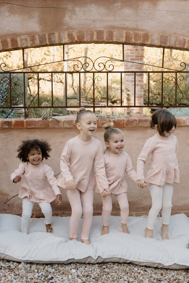 four young children wearing Mini Ribbed leggings in Available Colours, standing and playing with a decorative fence in the background.